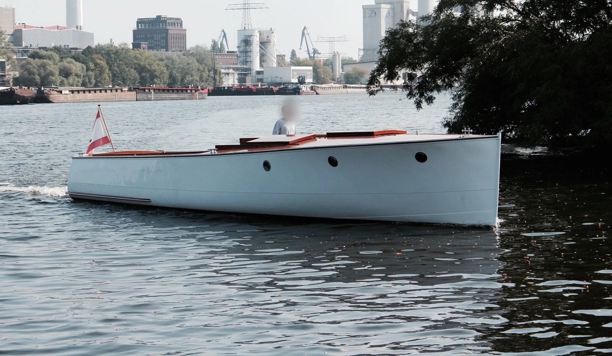 Die weiße Backdeck-Motoryacht Ara auf Berliner Gewässern vor einem Industriepanorama.